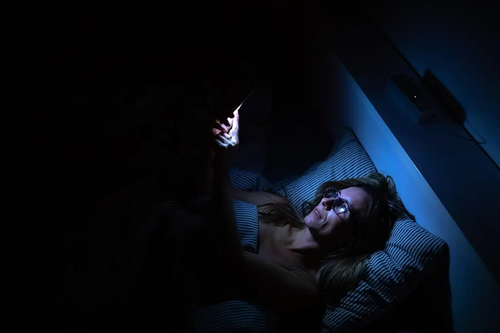 woman laying in bed scrolling on her phone in the dark